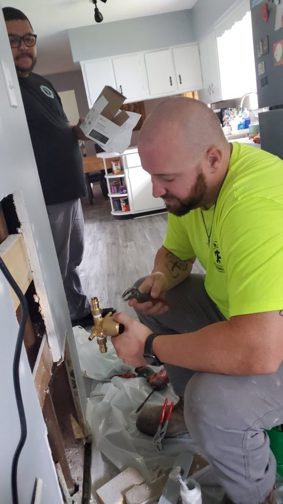 Plumber working on pipes through a hole in the wall