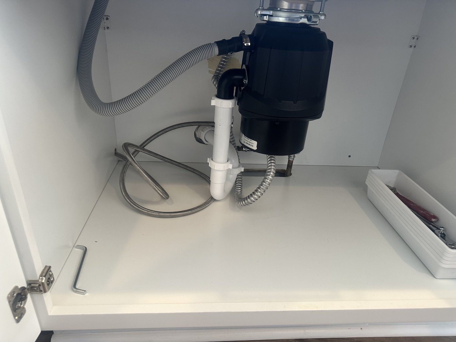 Black garbage disposal installed under white cabinet.