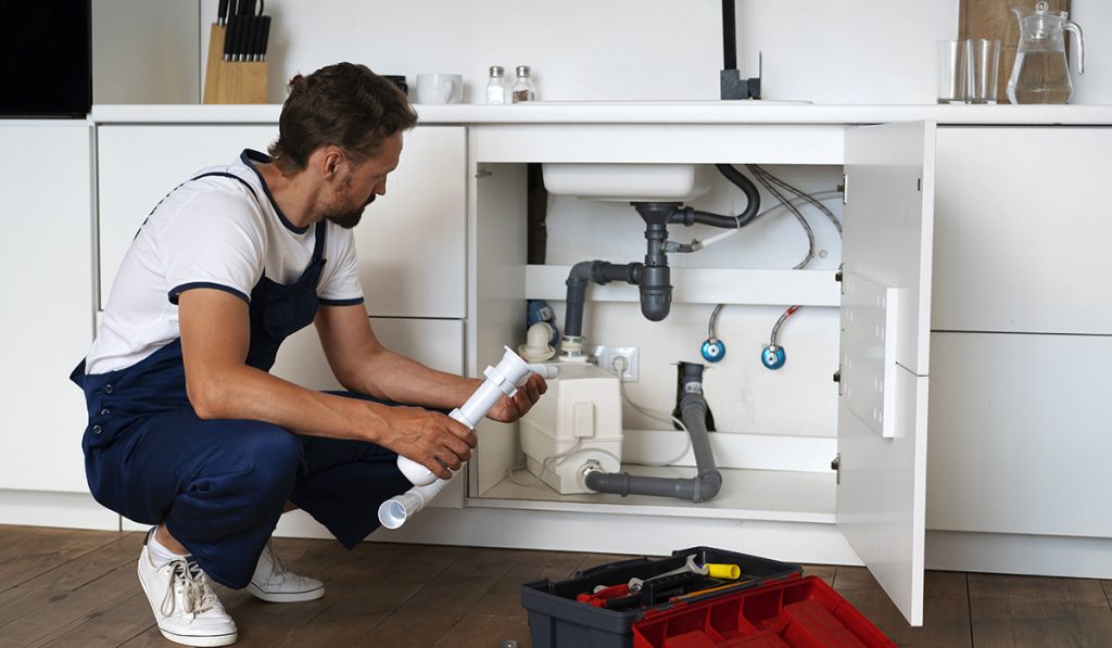 Plumber inspecting under-sink pipes and drainage system while diagnosing common kitchen plumbing problems.