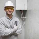Plumbing expert standing beside a newly installed tankless water heater unit.