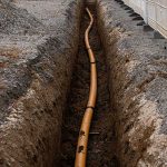 An exposed underground pipe with fittings surrounded by soil, illustrating vulnerability to shifting ground and soil movement.