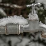 Snow-covered outdoor faucet and water pipe showing winter conditions that can lead to frozen plumbing lines.