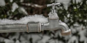 Snow-covered outdoor faucet and water pipe showing winter conditions that can lead to frozen plumbing lines.