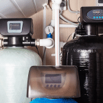 Residential water treatment setup showing dual tank water softener system with digital control heads and plumbing connections.