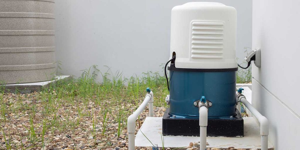 An outdoor blue and white automatic well water pump system experiencing short cycling issues installed next to a residential house.