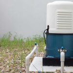 An outdoor blue and white automatic well water pump system experiencing short cycling issues installed next to a residential house.