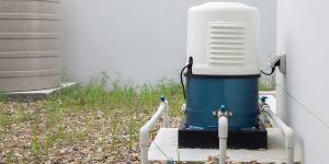 An outdoor blue and white automatic well water pump system experiencing short cycling issues installed next to a residential house.