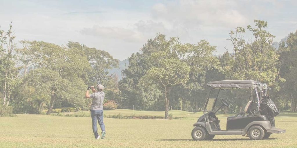 Golfer taking a swing on a scenic green course with a golf cart nearby during the annual Foundation Fest event.
