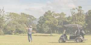 Golfer taking a swing on a scenic green course with a golf cart nearby during the annual Foundation Fest event.
