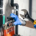 Plumber holding an adjustable wrench while inspecting pipe valves as part of an essential plumbing maintenance guide for homeowners.