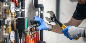 Plumber holding an adjustable wrench while inspecting pipe valves as part of an essential plumbing maintenance guide for homeowners.